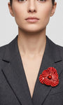 Vista frontal del maxibroche floral rojo de Ciléa Paris prendido en la solapa de una chaqueta de traje gris oscura, detallando su volumen y relieve.