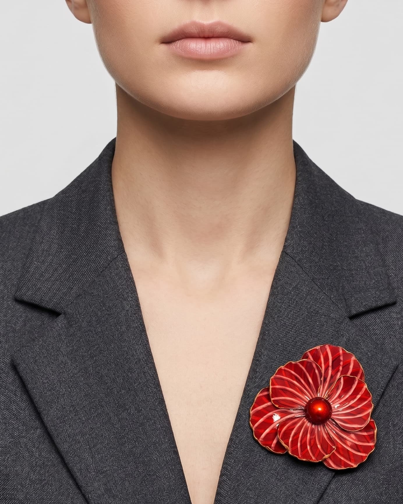 Vista frontal del maxibroche floral rojo de Ciléa Paris prendido en la solapa de una chaqueta de traje gris oscura, detallando su volumen y relieve.
