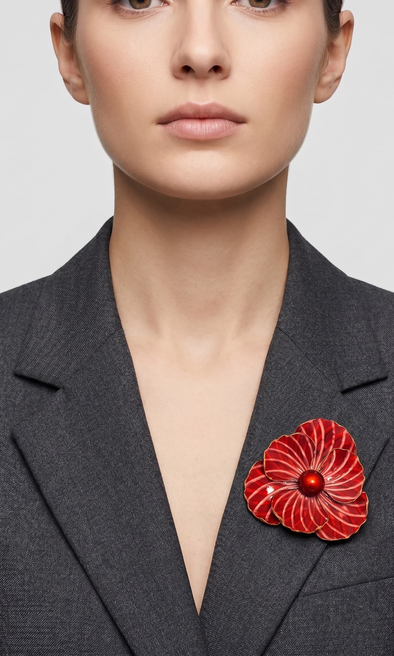 Vista frontal del maxibroche floral rojo de Ciléa Paris prendido en la solapa de una chaqueta de traje gris oscura, detallando su volumen y relieve.