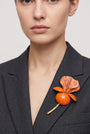 Vista frontal del gran broche floral naranja de Ciléa Paris colocado sobre la solapa de una chaqueta de traje gris oscura, detallando su escala XL y su volumen tridimensional.