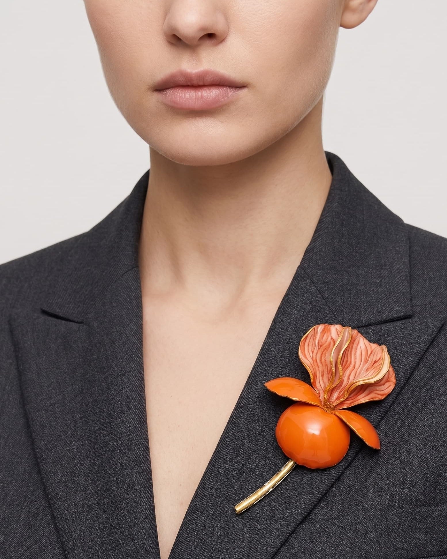 Vista frontal del gran broche floral naranja de Ciléa Paris colocado sobre la solapa de una chaqueta de traje gris oscura, detallando su escala XL y su volumen tridimensional.