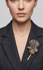 Vista frontal del maxibroche floral gris y oro de Ciléa Paris prendido en la solapa de un abrigo de traje gris oscuro, detallando su volumen tridimensional.