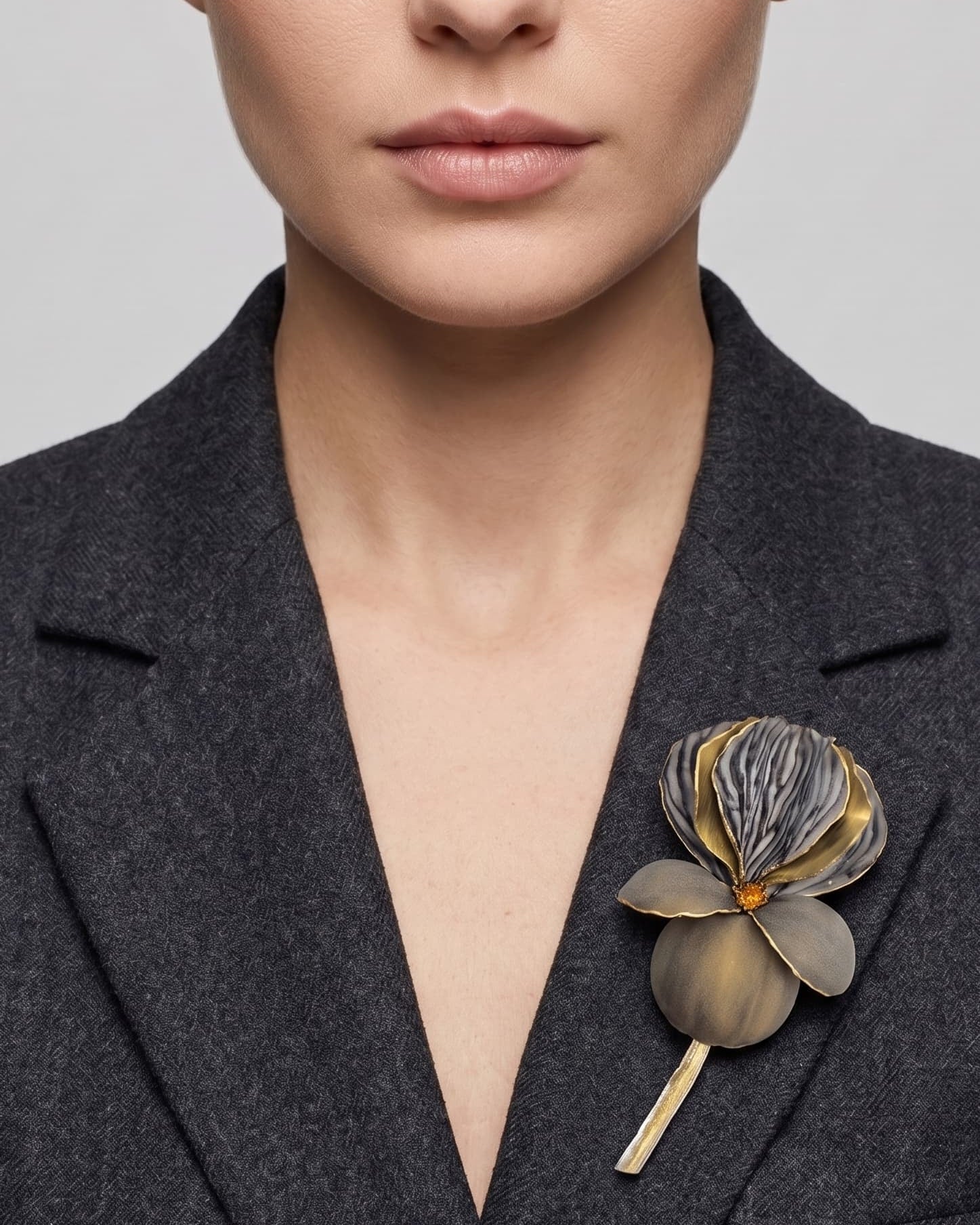 Vista frontal del maxibroche floral gris y oro de Ciléa Paris prendido en la solapa de un abrigo de traje gris oscuro, detallando su volumen tridimensional.
