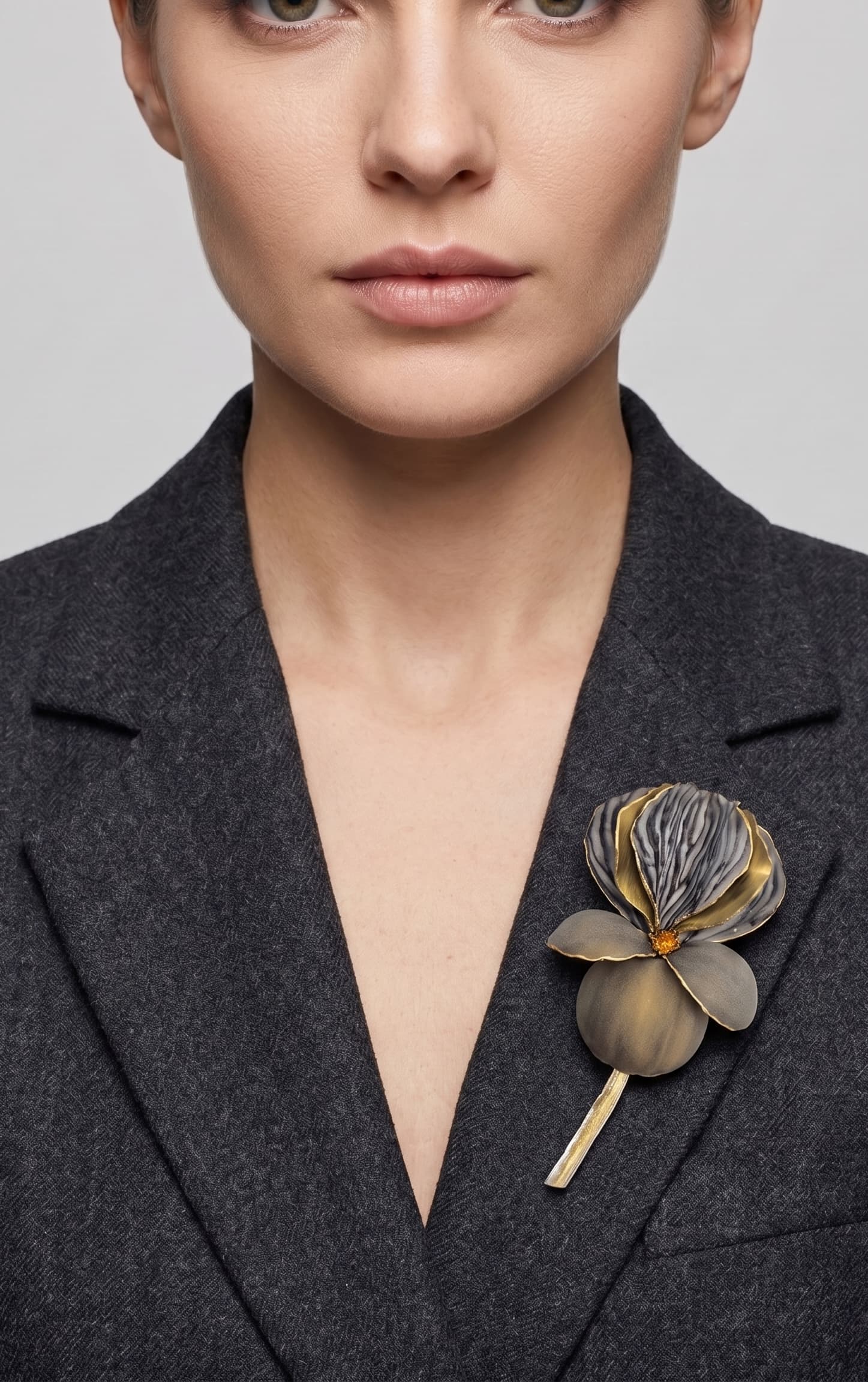 Vista frontal del maxibroche floral gris y oro de Ciléa Paris prendido en la solapa de un abrigo de traje gris oscuro, detallando su volumen tridimensional.