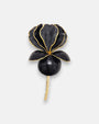 Broche mediano en forma de flor iris de Ciléa Paris, mostrando sus pétalos en negro azabache de acabado brillante, finos perfiles en oro y tallo dorado.