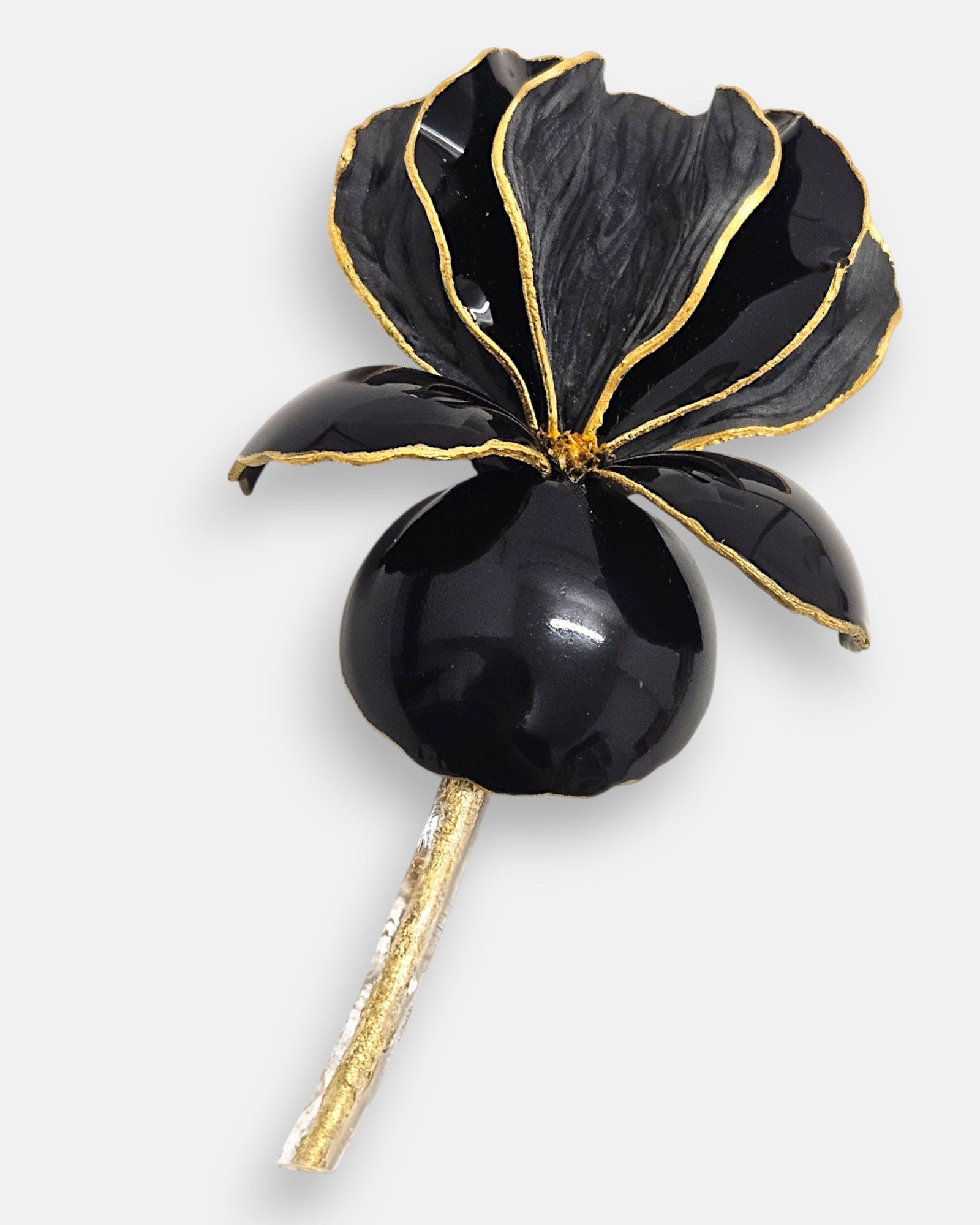 Primer plano macro de la flor artesanal de Ciléa Paris, detallando el pulido de los pétalos esmaltados negros y los destellos del contorno en oro brillante.