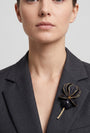 Vista frontal del maxibroche floral negro de Ciléa Paris prendido en la solapa de una chaqueta de traje gris, detallando su volumen y relieve tridimensional.