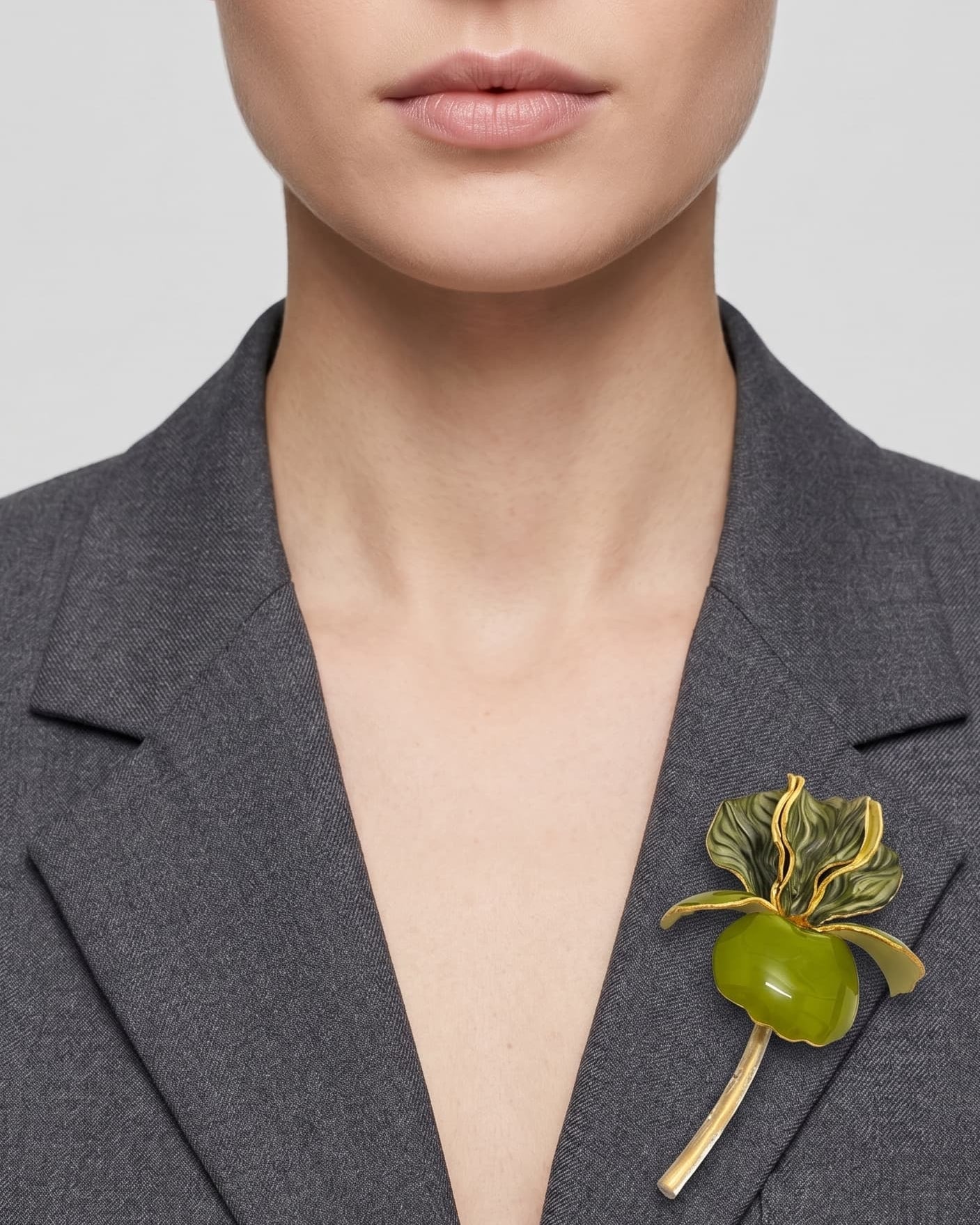 Vista frontal del maxibroche floral verde de Ciléa Paris prendido en la solapa de una chaqueta de traje gris oscuro, detallando su escala y volumen tridimensional.