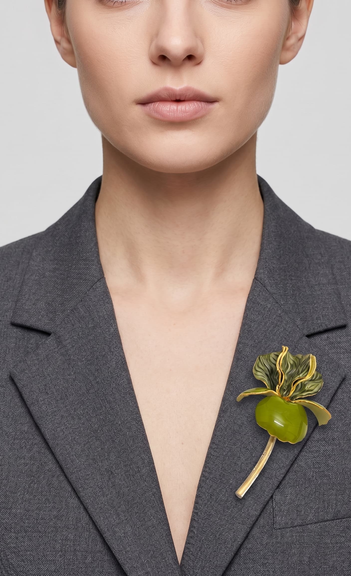 Vista frontal del maxibroche floral verde de Ciléa Paris prendido en la solapa de una chaqueta de traje gris oscuro, detallando su escala y volumen tridimensional.