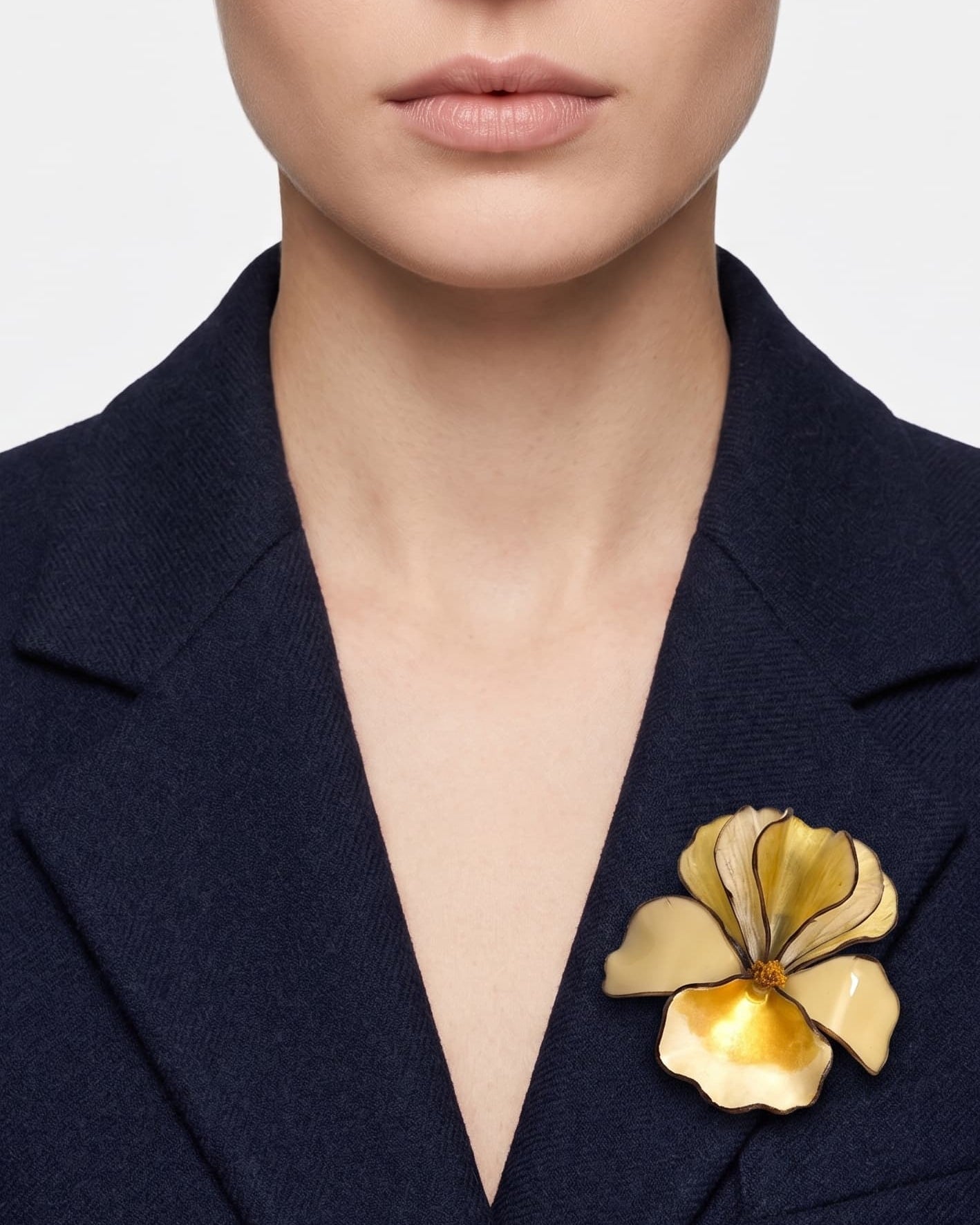 Vista frontal del broche floral crema de Ciléa Paris prendido en la solapa de una americana de traje azul marino, detallando su relieve tridimensional.
