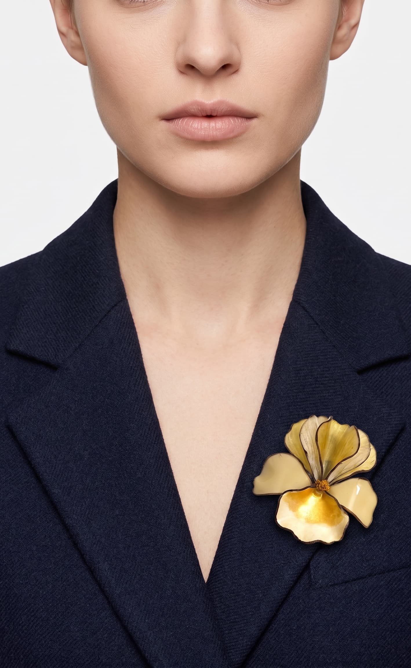 Vista frontal del broche floral crema de Ciléa Paris prendido en la solapa de una americana de traje azul marino, detallando su relieve tridimensional.