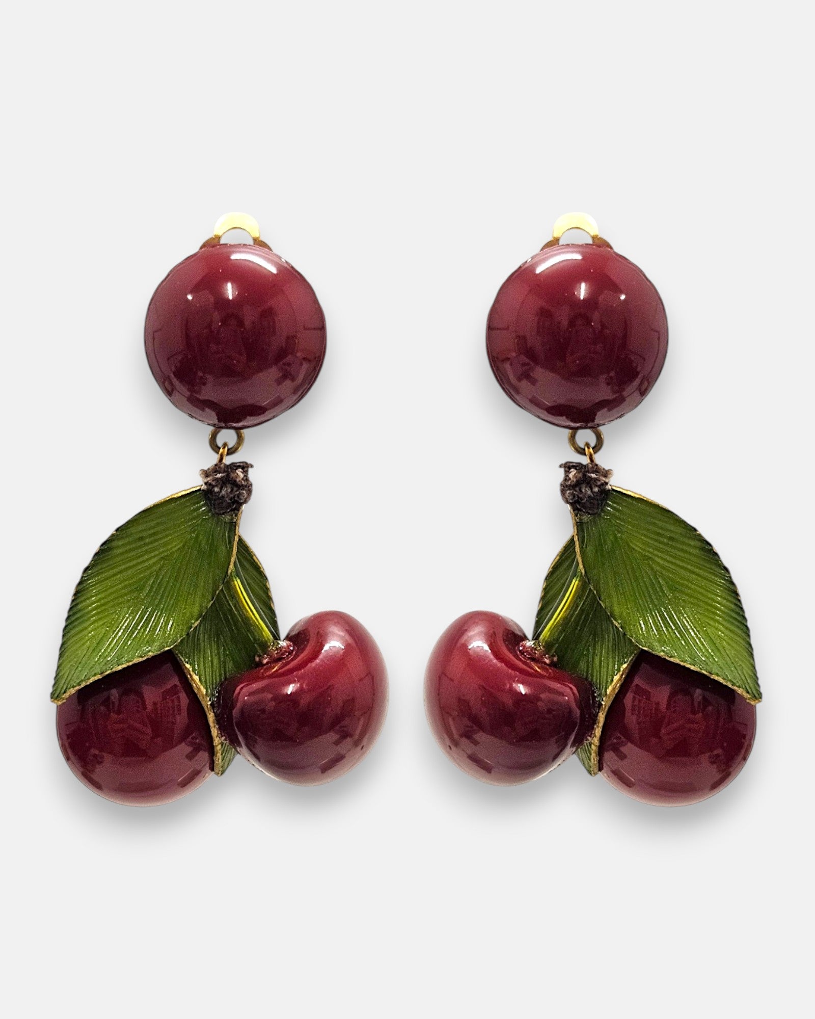 Pareja de pendientes grandes de Ciléa Paris con diseño de cerezas dobles en color rojo guinda esmaltado, hojas verdes brillantes y botón superior redondo.