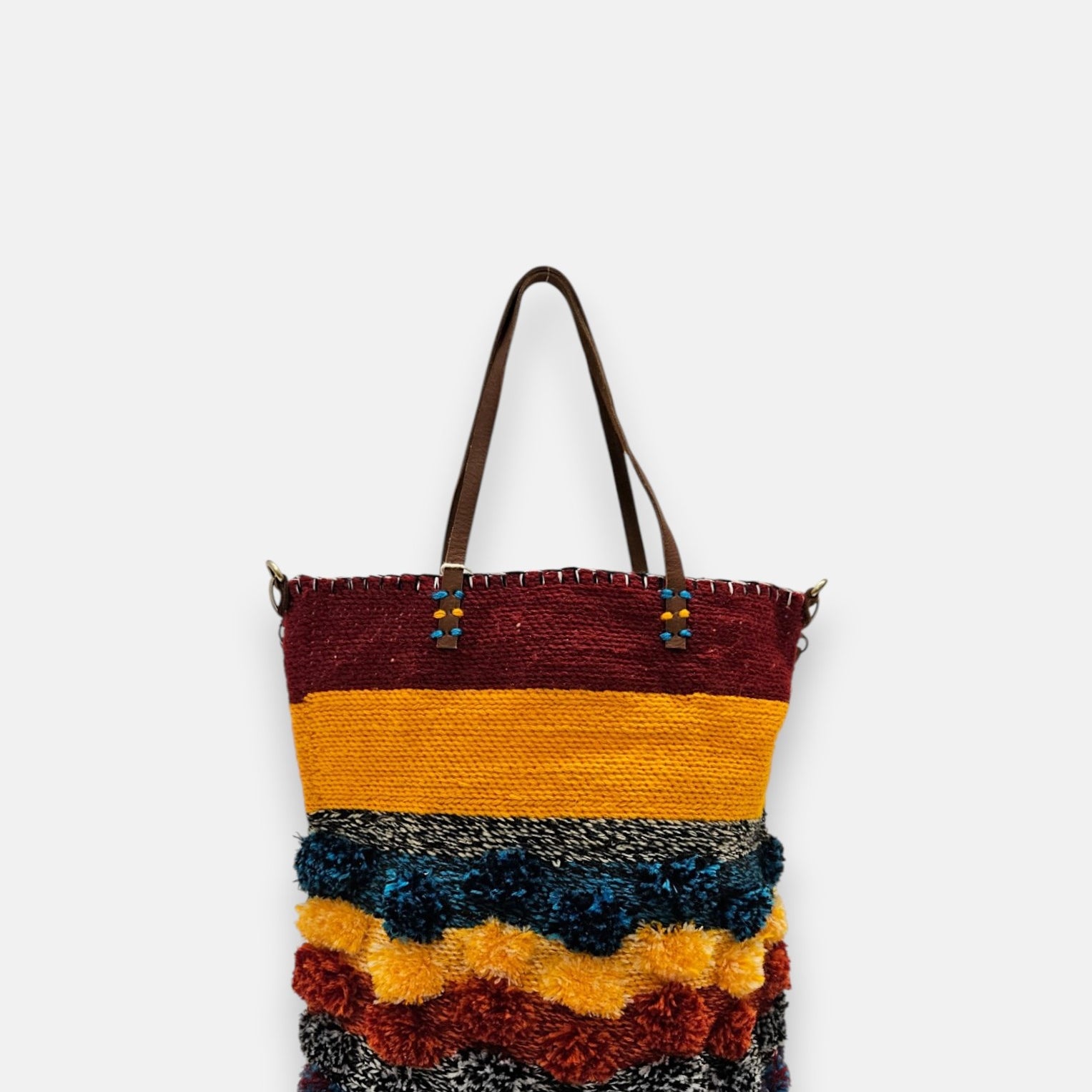 Bolso artesanal de material reciclado con franjas amarillas, granates y pompones azules y naranjas.