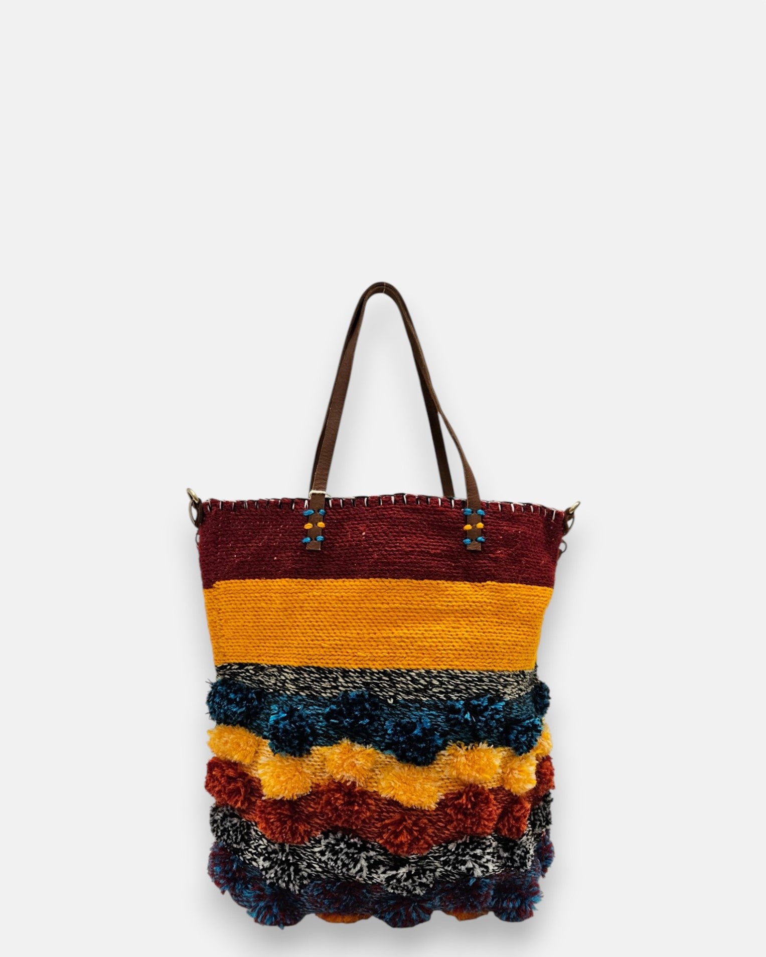 Bolso artesanal de material reciclado con franjas amarillas, granates y pompones azules y naranjas.