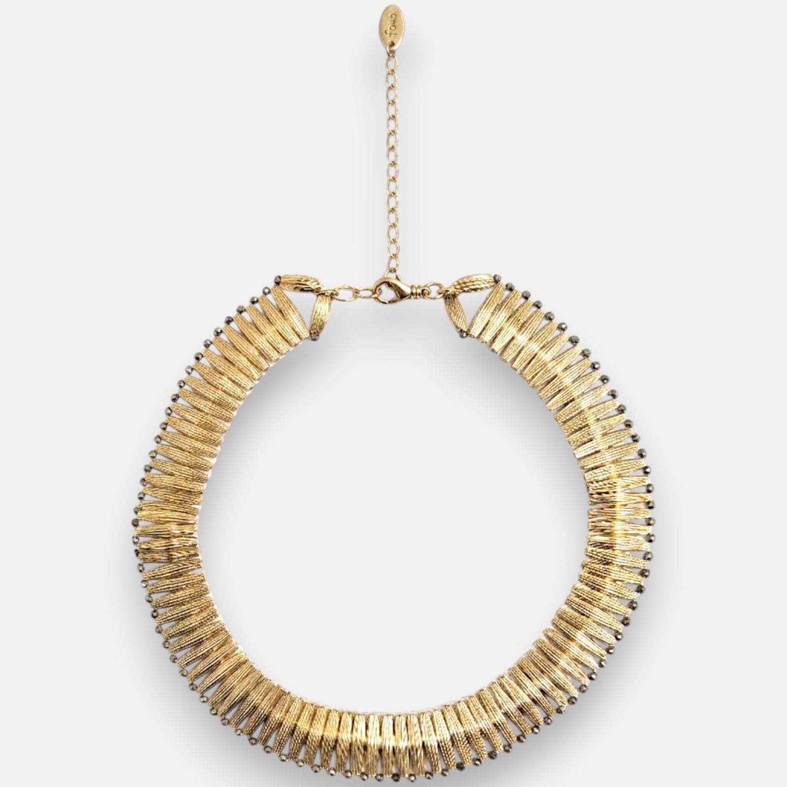 Collar gargantilla rígida Tataborello de diseño radial plisado en color oro con borde de cuentas oscuras y cadena alargadora con medalla de la marca.