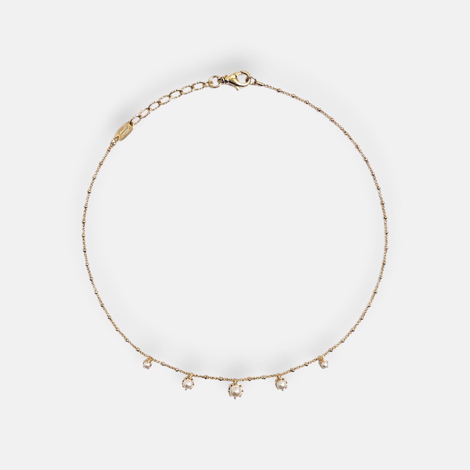 Collar de cadena fina dorada Tataborello extendido en círculo con cinco pequeñas perlas colgantes en la parte inferior y cierre ajustable de mosquetón.