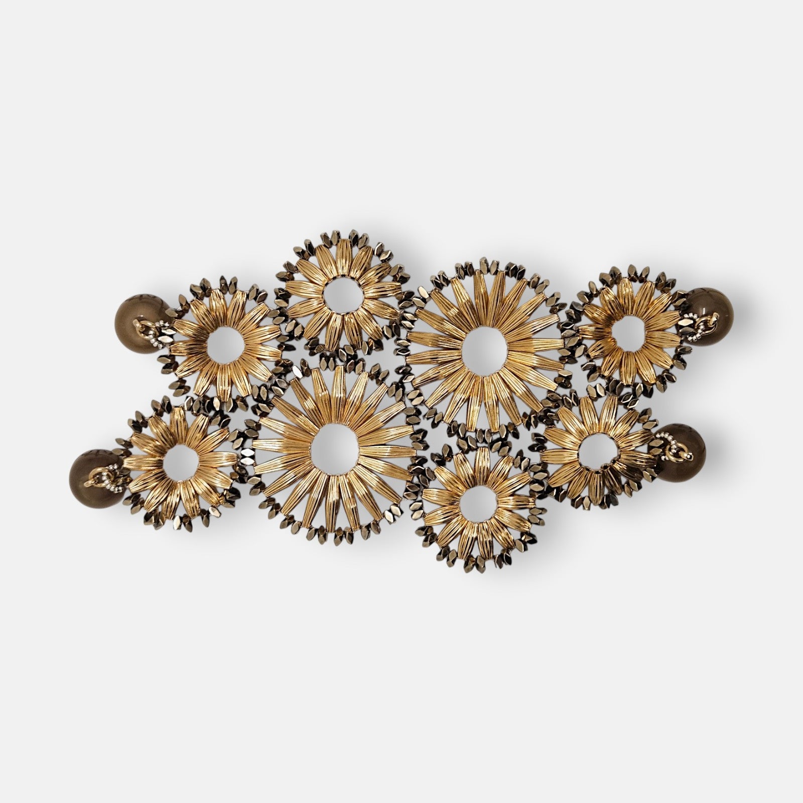 Maxi pulsera ancha Tataborello extendida con un diseño calado de soles dorados estriados y doble cierre magnético.