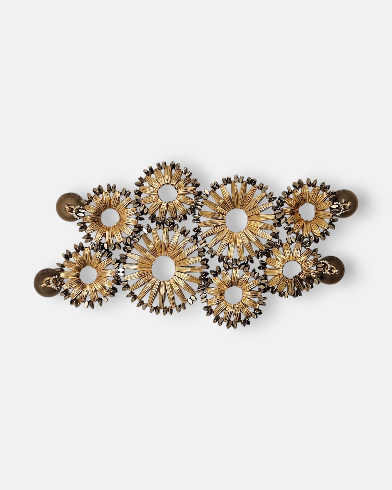 Maxi pulsera ancha Tataborello extendida con un diseño calado de soles dorados estriados y doble cierre magnético.