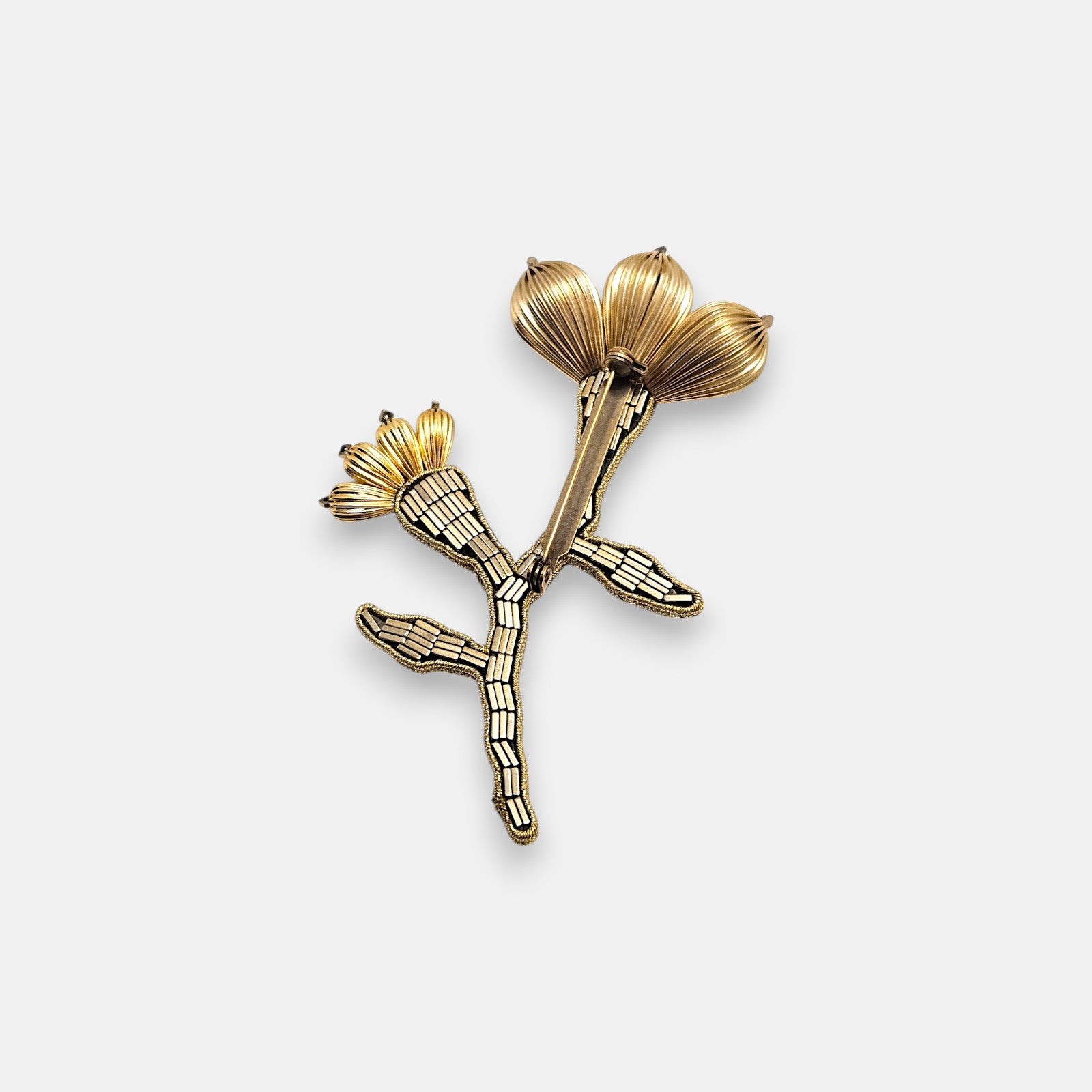 Broche artesanal de solapa Tataborello con silueta de flor y rama bordada en canutillos bronce y pétalos de oro estriados.