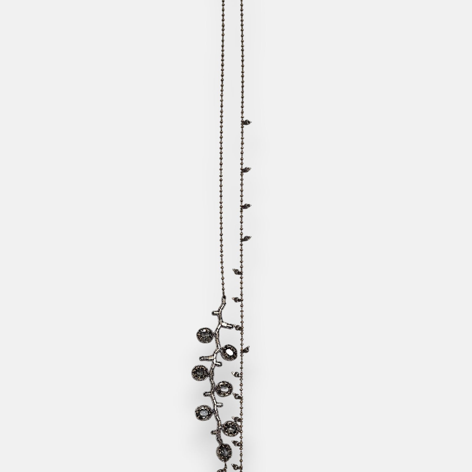 Collar largo sautoir Tataborello extendido en vertical mostrando su cadena fina de bolitas oscuras con dijes colgantes y una rama lateral de cristales gris ahumado.