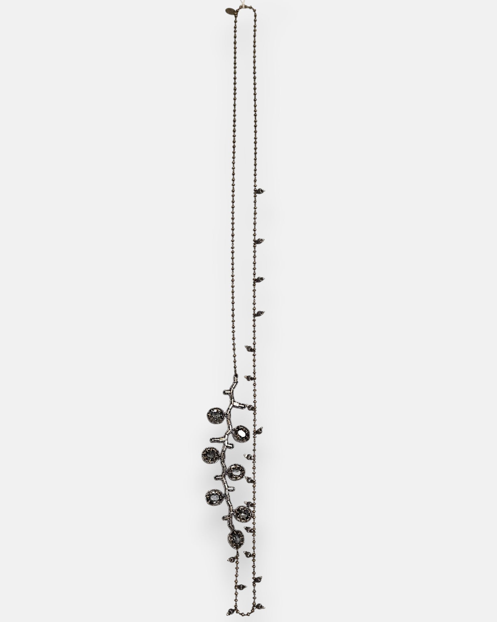 Collar largo sautoir Tataborello extendido en vertical mostrando su cadena fina de bolitas oscuras con dijes colgantes y una rama lateral de cristales gris ahumado.