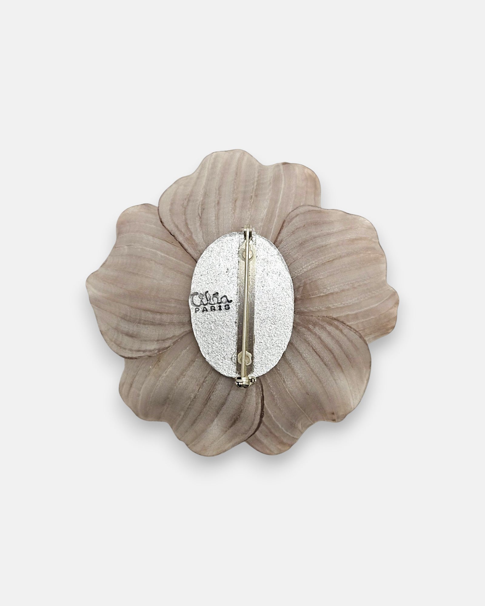 parte trasera del broche floral, enseñando la placa metálica ovalada grabada con el logotipo de Ciléa Paris y el alfiler de cierre de seguridad.