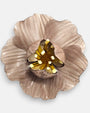 primer plano del broche artesanal de Ciléa Paris, enfocando los reflejos nacarados de los pétalos modelados y la profundidad translúcida de su centro dorado.
