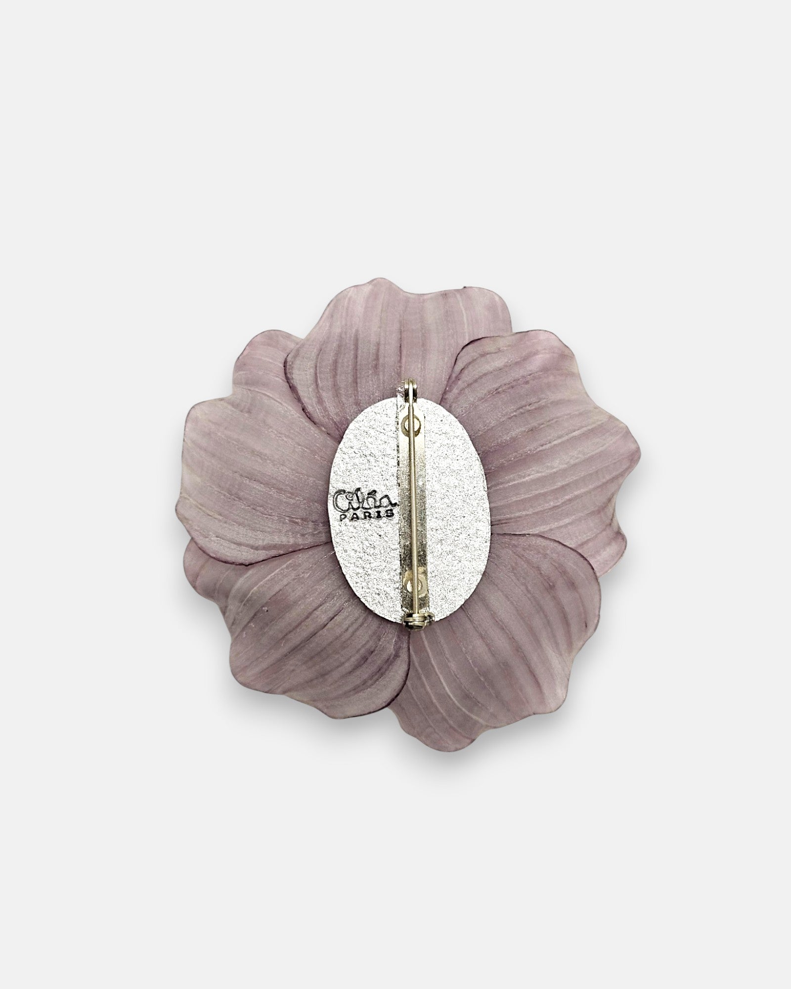 parte trasera del broche floral, enseñando la placa metálica ovalada grabada con el logotipo de Ciléa Paris y el alfiler de cierre de seguridad.