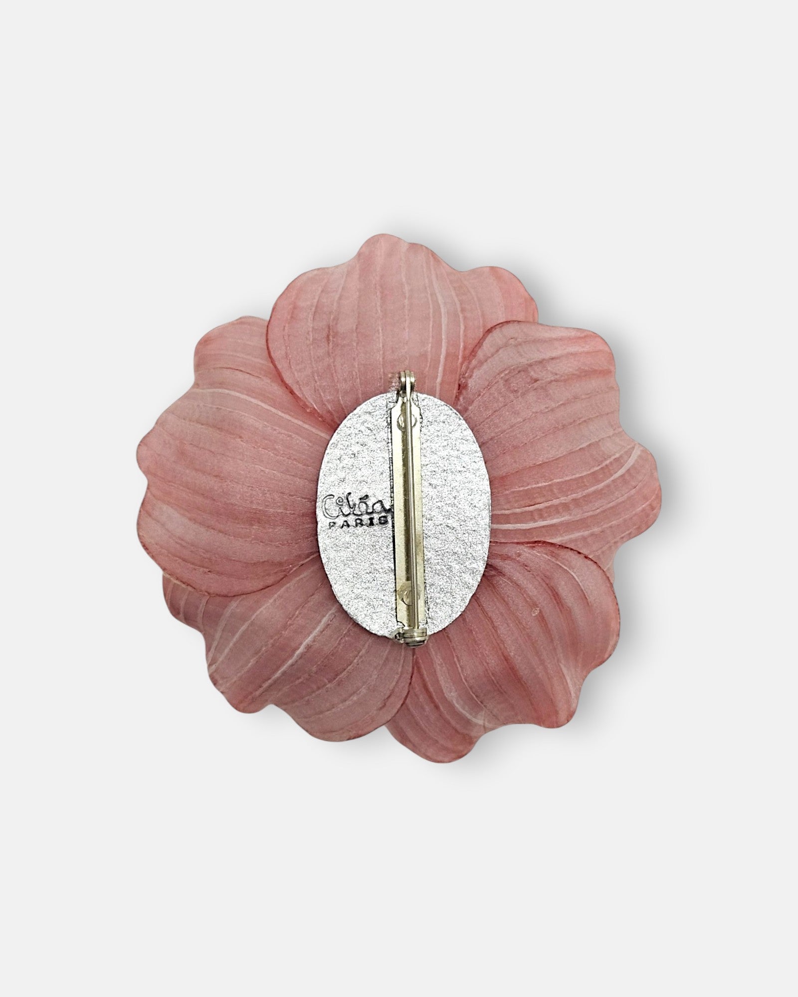 parte trasera del broche floral, enseñando la placa metálica ovalada grabada con el logotipo de Ciléa Paris y el alfiler de cierre de seguridad.