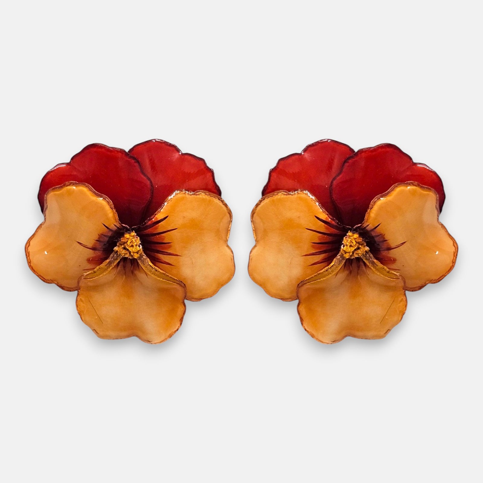 pareja de pendientes con forma de flor de pensamiento de Ciléa Paris, destacando sus pétalos superiores rojo borgoña y sus pétalos inferiores en tono ocre o melocotón brillante.