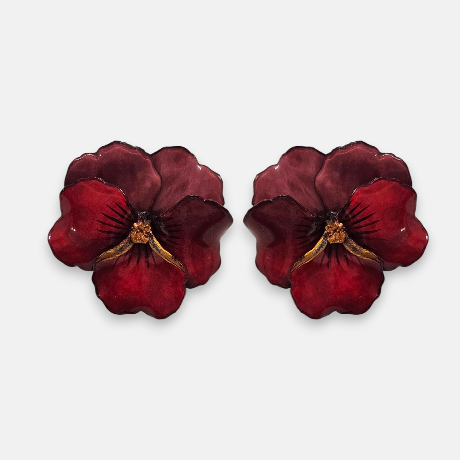 pareja de pendientes con forma de flor de pensamiento de Ciléa Paris, destacando sus pétalos superiores en color ciruela oscuro y sus pétalos inferiores en rojo brillante con acabado pulido.