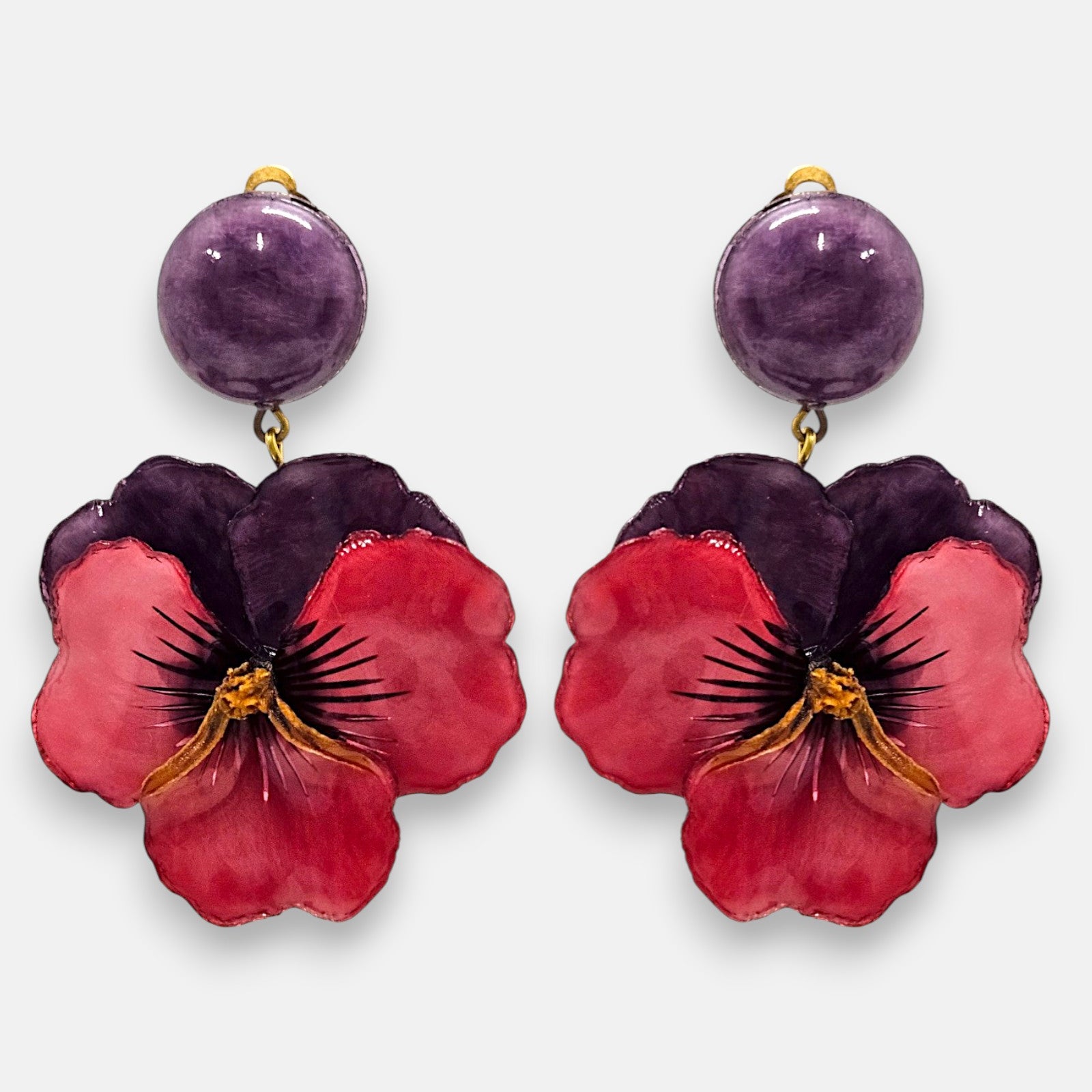 pareja de pendientes colgantes maxi con forma de flor de pensamiento de Ciléa Paris, destacando sus pétalos superiores en color violeta oscuro, pétalos inferiores en rojo rubí brillante y un gran botón superior esférico a juego con enganche de pinza.
