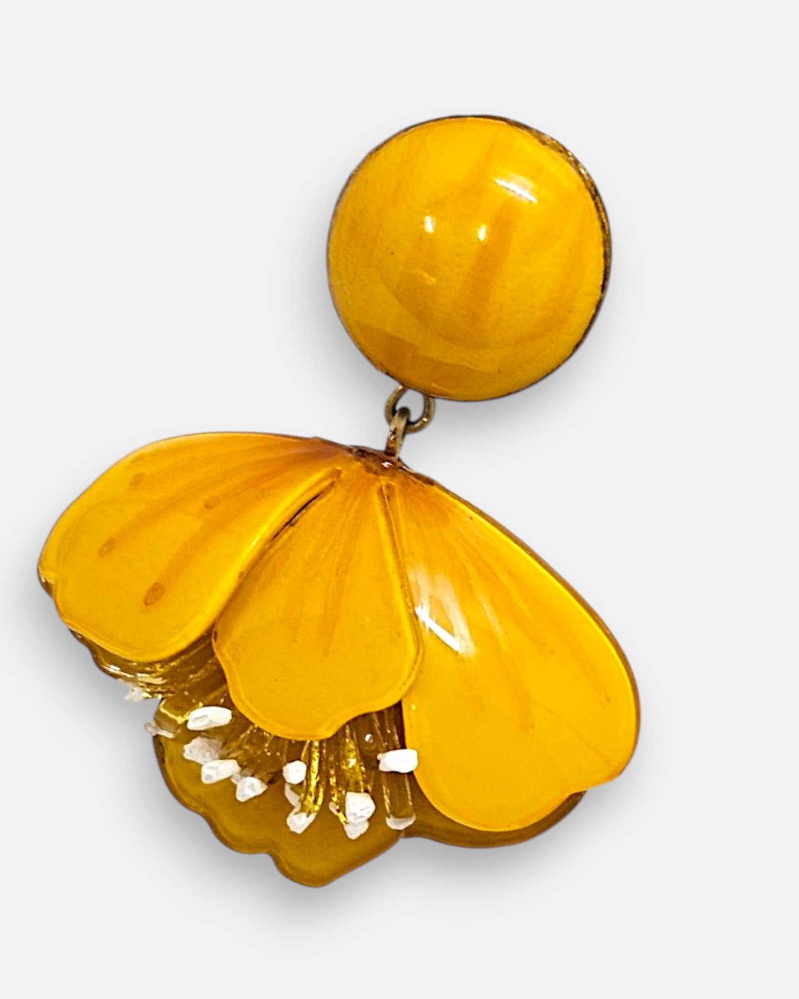 primer plano de la flor esmaltada de Ciléa Paris, enfocando el matiz translúcido color ámbar, las vetas sutiles de los pétalos y el conjunto inferior de pistilos texturizados en blanco y dorado.