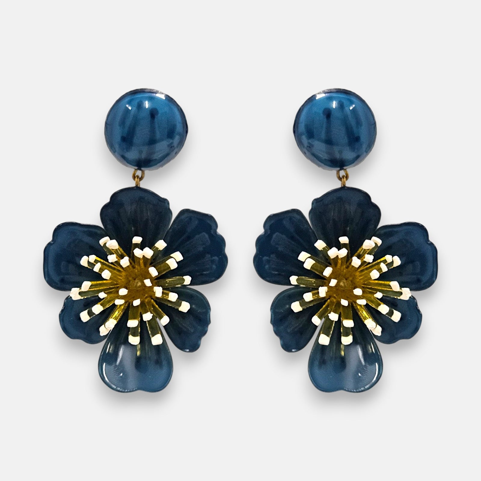 pareja de pendientes colgantes maxi con forma de flor de anémona de Ciléa Paris, destacando sus pétalos de resina en color azul petróleo brillante, un complejo centro de pistilos dorados con puntas blancas y un botón superior esférico de perno coordinado.