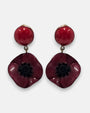 pareja de pendientes colgantes mini con silueta de flor de amapola de Ciléa Paris, destacando sus pétalos de resina en color rojo burdeos brillante, el centro negro texturizado que emula los estambres y un botón superior esférico de perno coordinado.