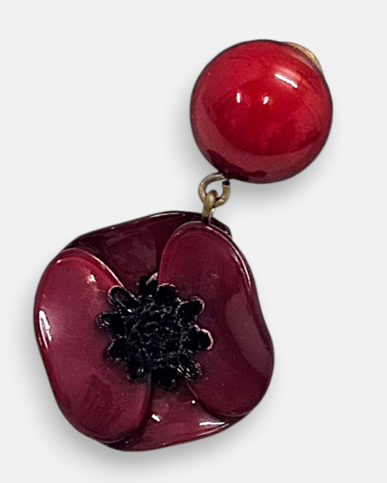 plano macro del pendiente de Ciléa Paris, enfocando el acabado brillante de los pétalos rojo burdeos, el centro negro texturizado que emula los estambres de la amapola y la esfera esmaltada del perno.