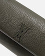 primer plano macro del Bolso Bandolera Verde Musgo de Plinio Visonà, permitiendo apreciar la textura del grano de la piel y el aplique del logotipo.