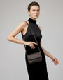modelo luciendo colgado al hombro el Bolso Bandolera Cacao de Plinio Visonà sobre un elegante vestido negro.