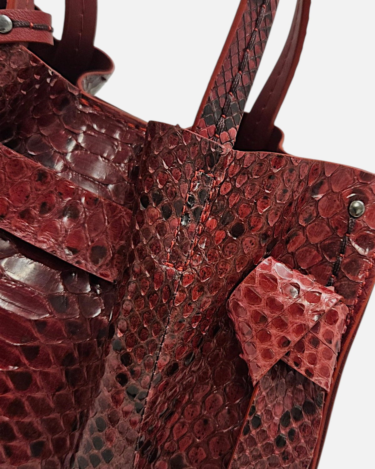 plano macro del grabado de escamas en piel burdeos y el detalle de la costura del nudo del Bolso Pitón Pitagora Bordeus de Plinio Visonà.
