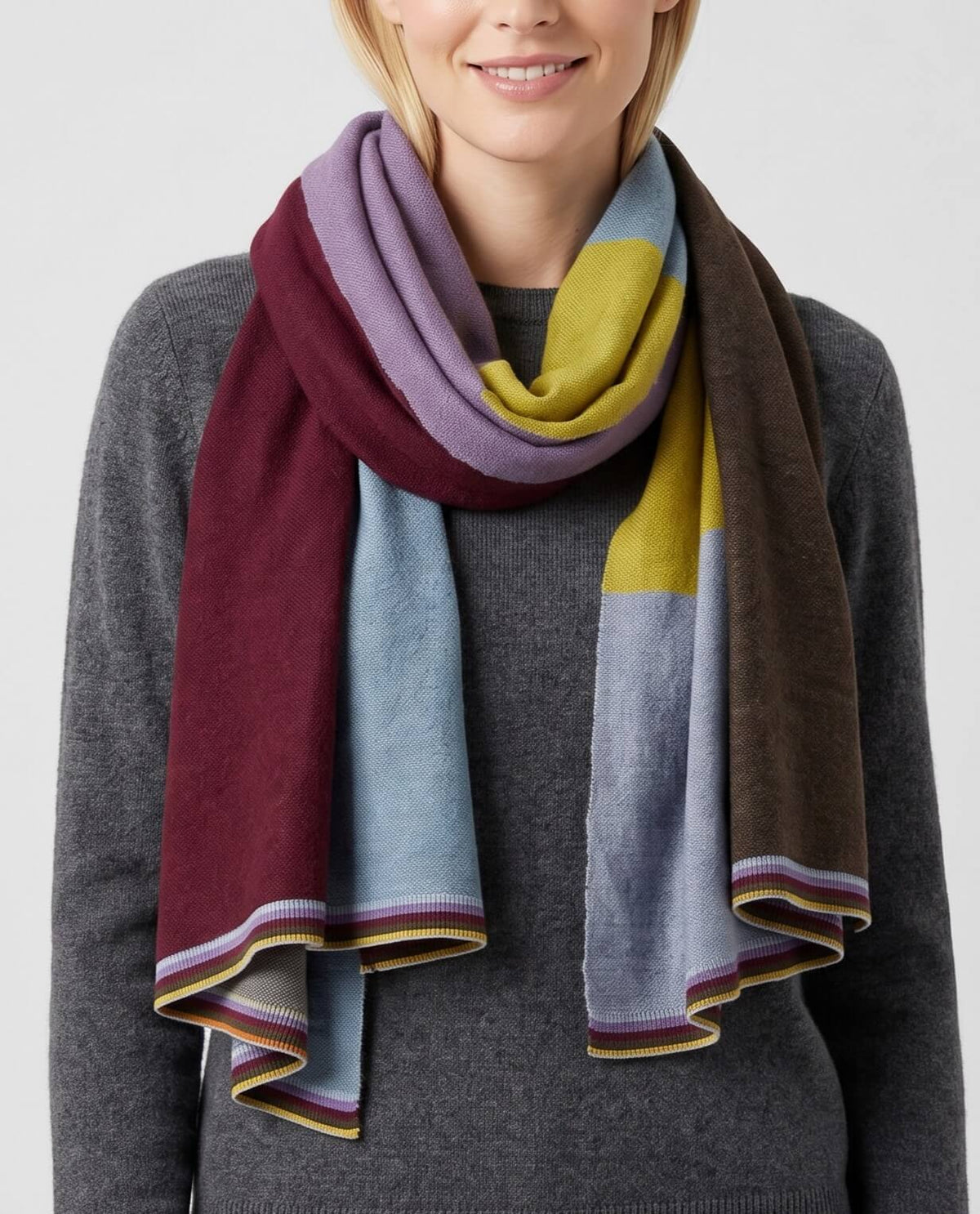  modelo luciendo el Foulard Blok Pastel anudado al cuello sobre un jersey gris, apreciando los bloques de color azul celeste, lavanda, burdeos y mostaza.   