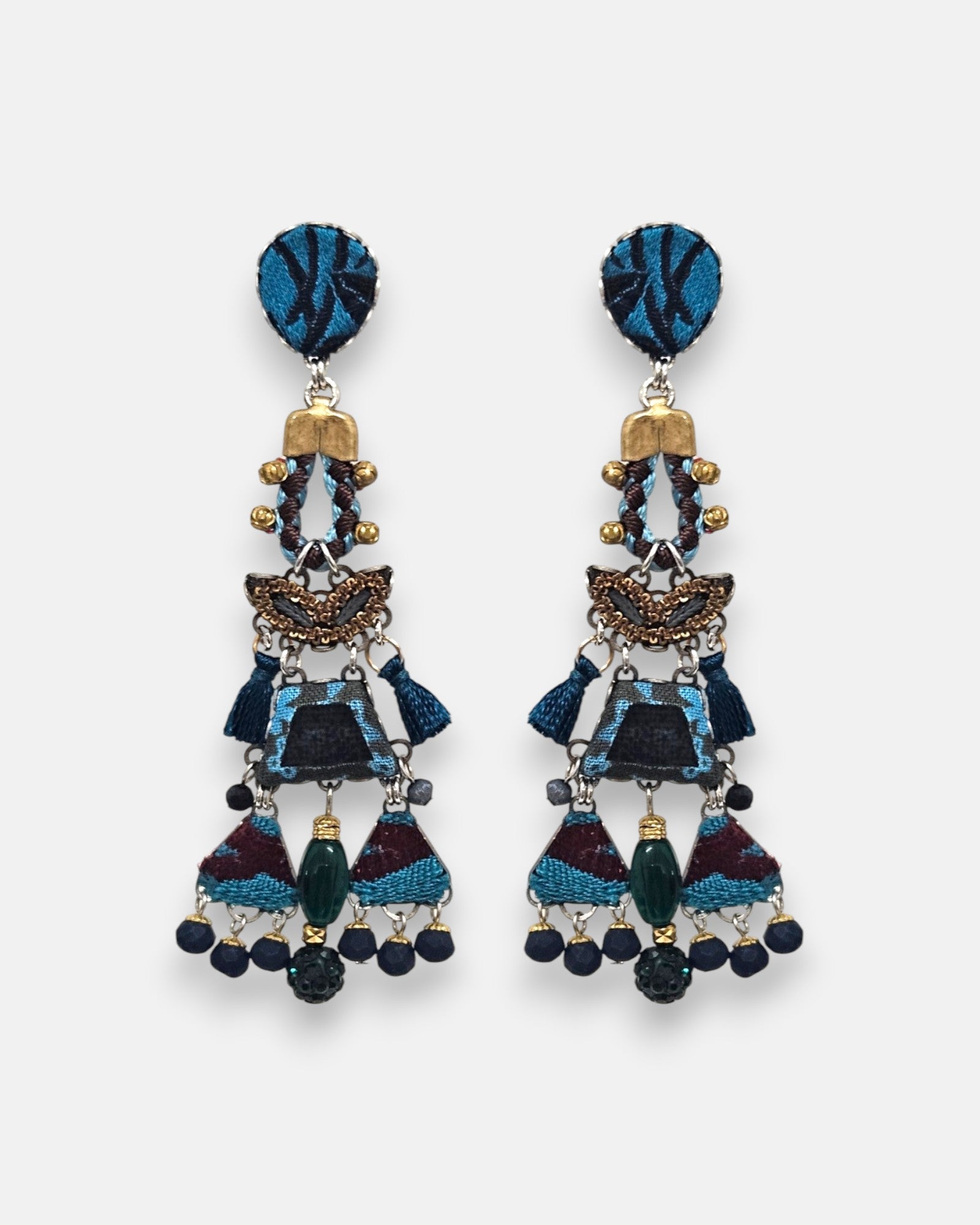 par de pendientes de frente sobre un fondo neutro, destacando su silueta alargada tipo chandelier con mosaicos en azul índigo, borlas y flecos de cuentas inferiores.
