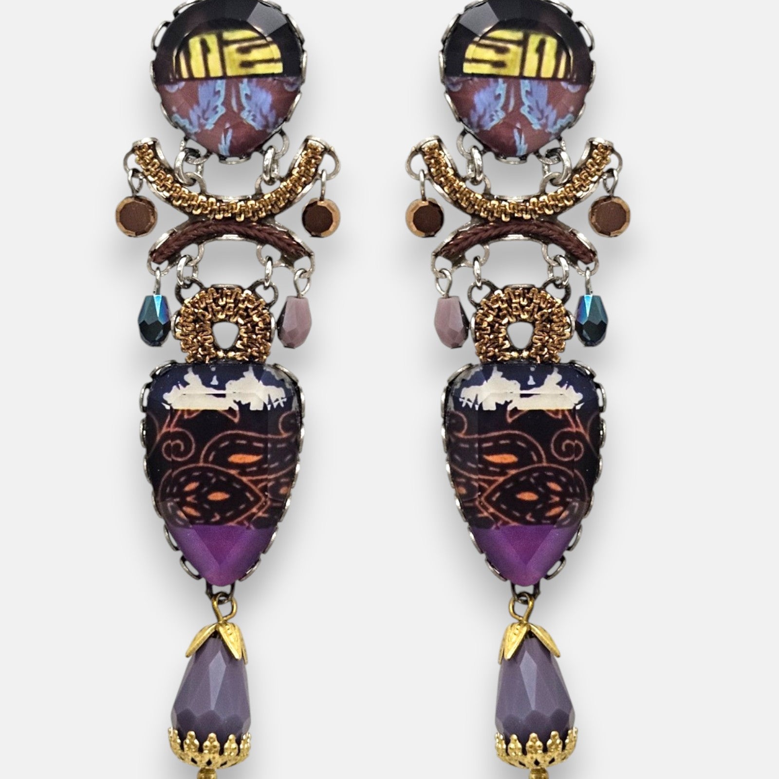 par de pendientes expuesto de frente sobre un fondo gris claro, destacando su silueta alargada de mosaico textil y la lágrima facetada malva inferior.