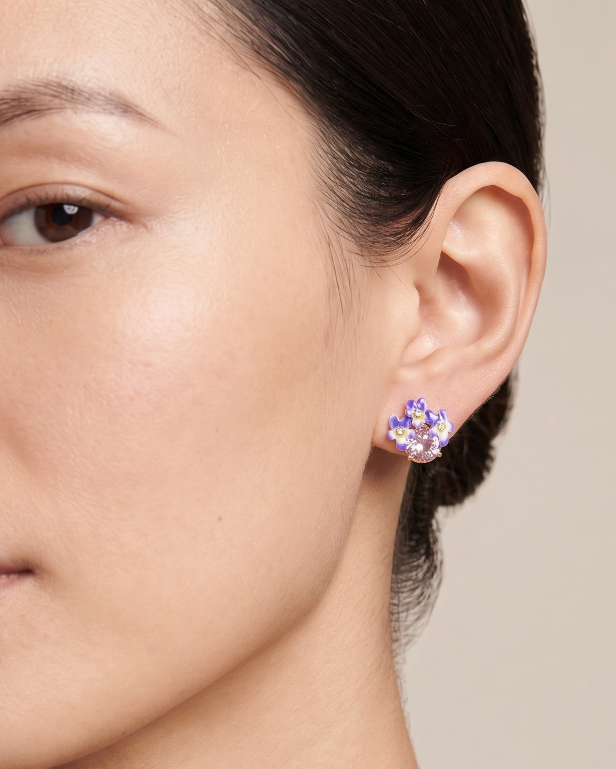 Modelo luciendo el pendiente de botón Les Néréides con flor de violeta esmaltada y cristal rosa ajustado en el lóbulo de la oreja.