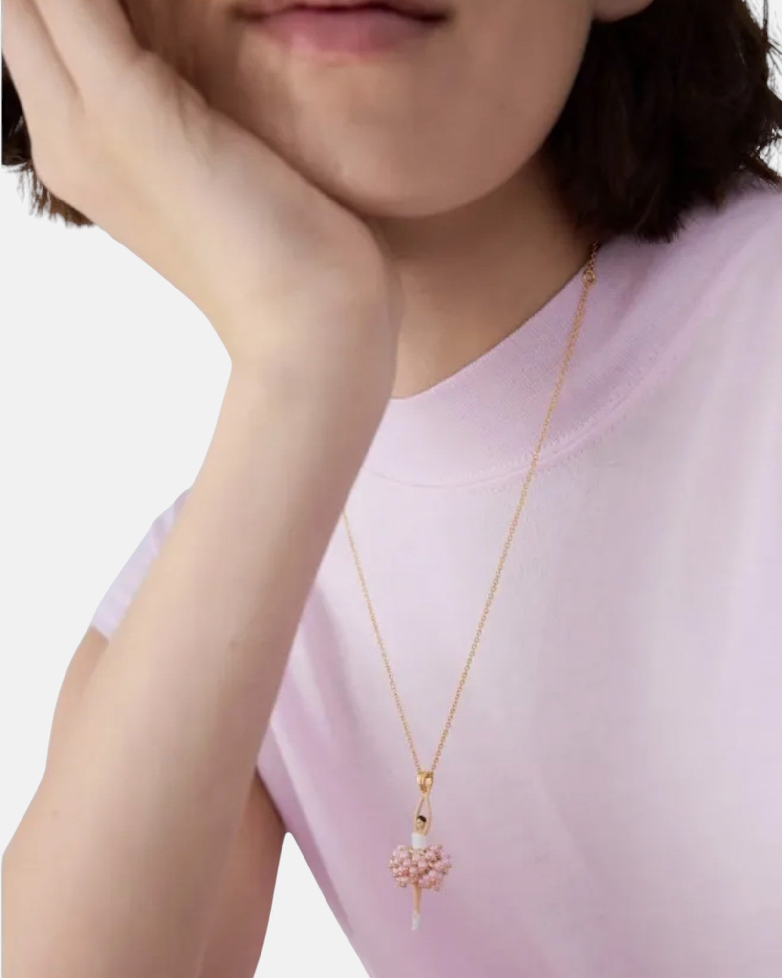 Modelo luciendo el collar fino Les Néréides Pas de Deux con colgante de bailarina en tutú rosa sobre camiseta pastel.