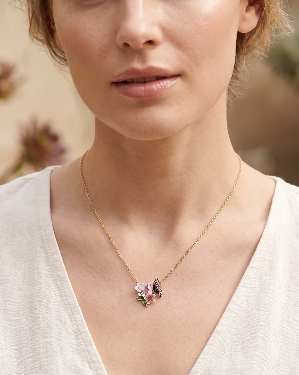 Modelo luciendo el collar Les Néréides Métamorphose Nocturne con colgante de mariposa y flores sobre una prenda blanca.
