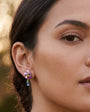 Modelo luciendo el pendiente asimétrico Les Néréides Violette Sauvage con flor de orquídea esmaltada y gota azul colgando sobre el lóbulo.