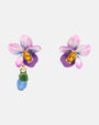 Par de pendientes asimétricos Les Néréides Violette Sauvage con orquídeas esmaltadas, cristales ámbar y gota de cristal azul sobre fondo neutro.