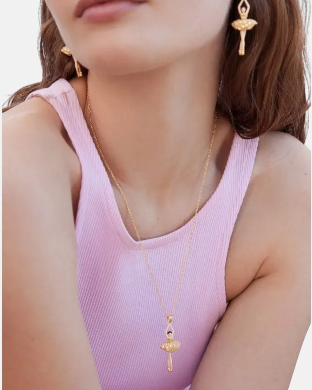 Modelo luciendo el collar de bailarina dorada Les Néréides Pas de Deux combinado con camiseta rosa y pendientes a juego.