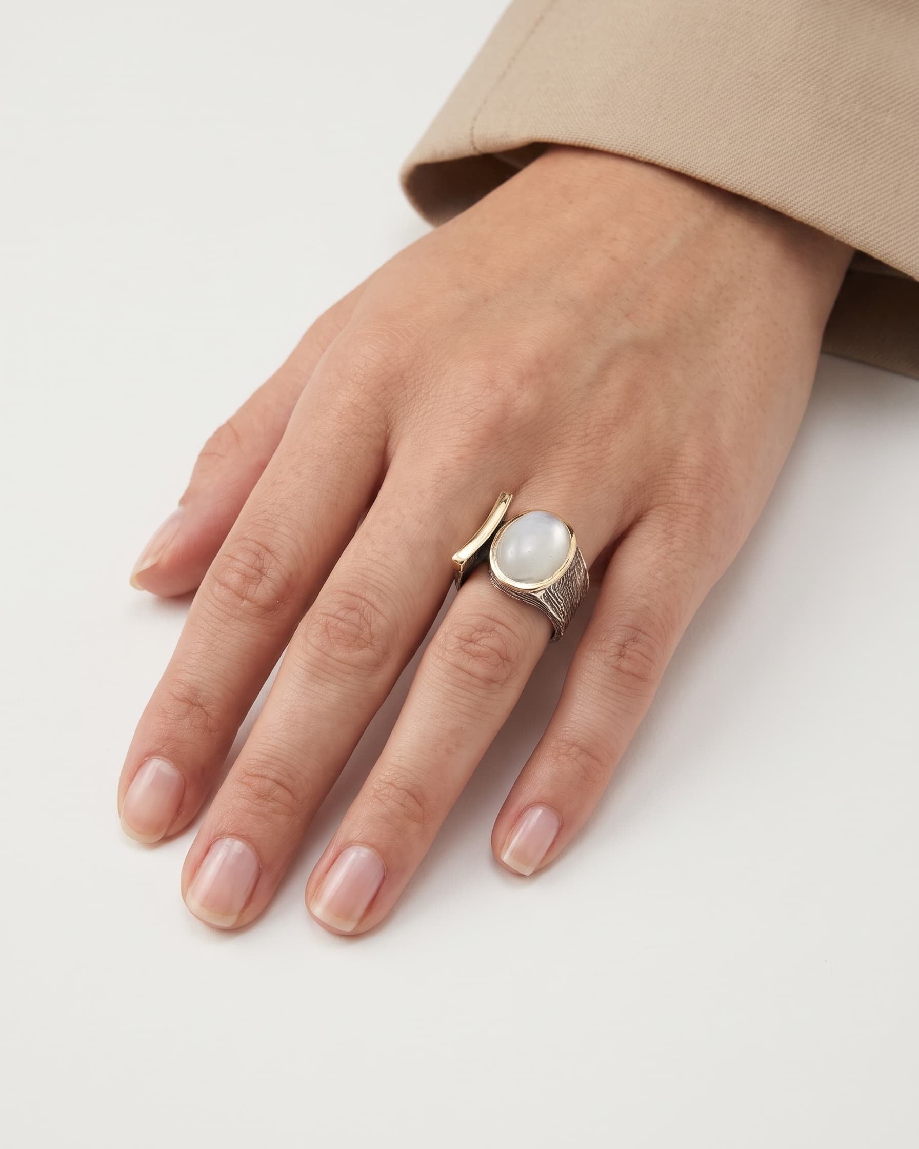 Anillo ancho de autor con cabujón blanco lechoso visto puesto en la mano de una modelo
