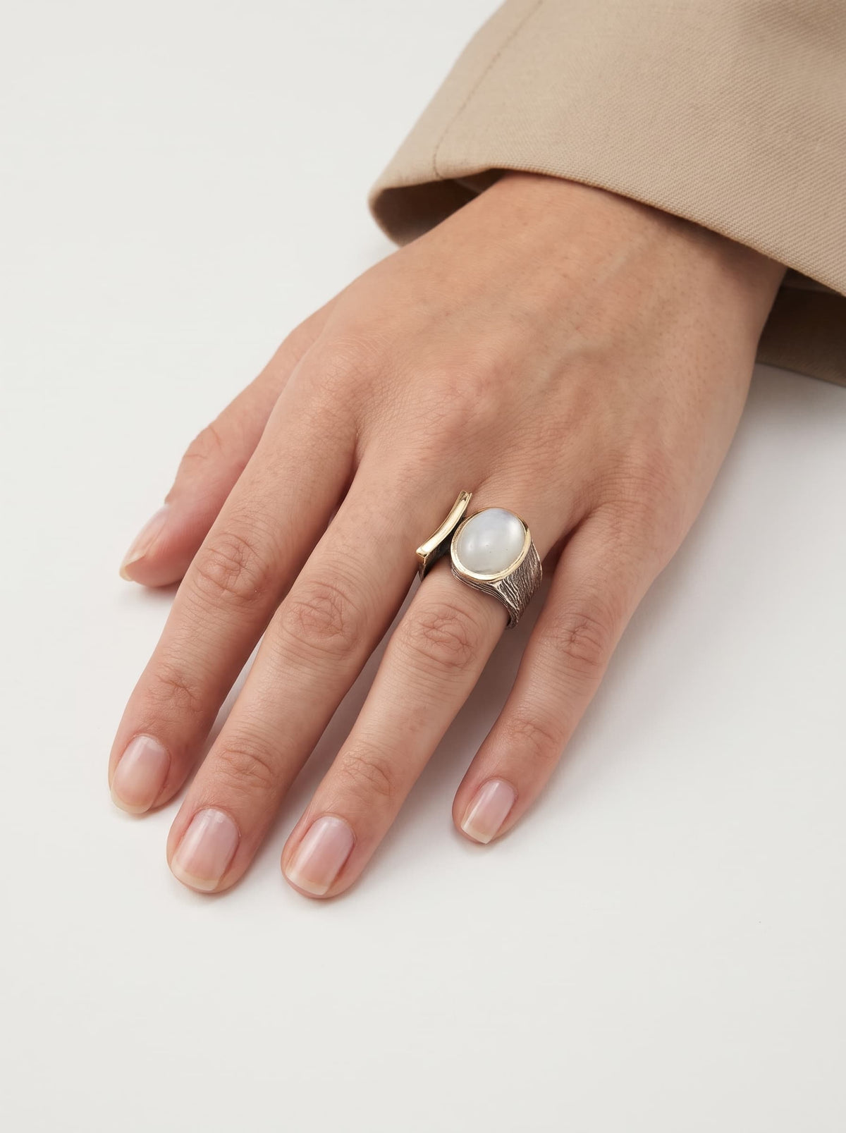 Anillo ancho de autor con cabujón blanco lechoso visto puesto en la mano de una modelo